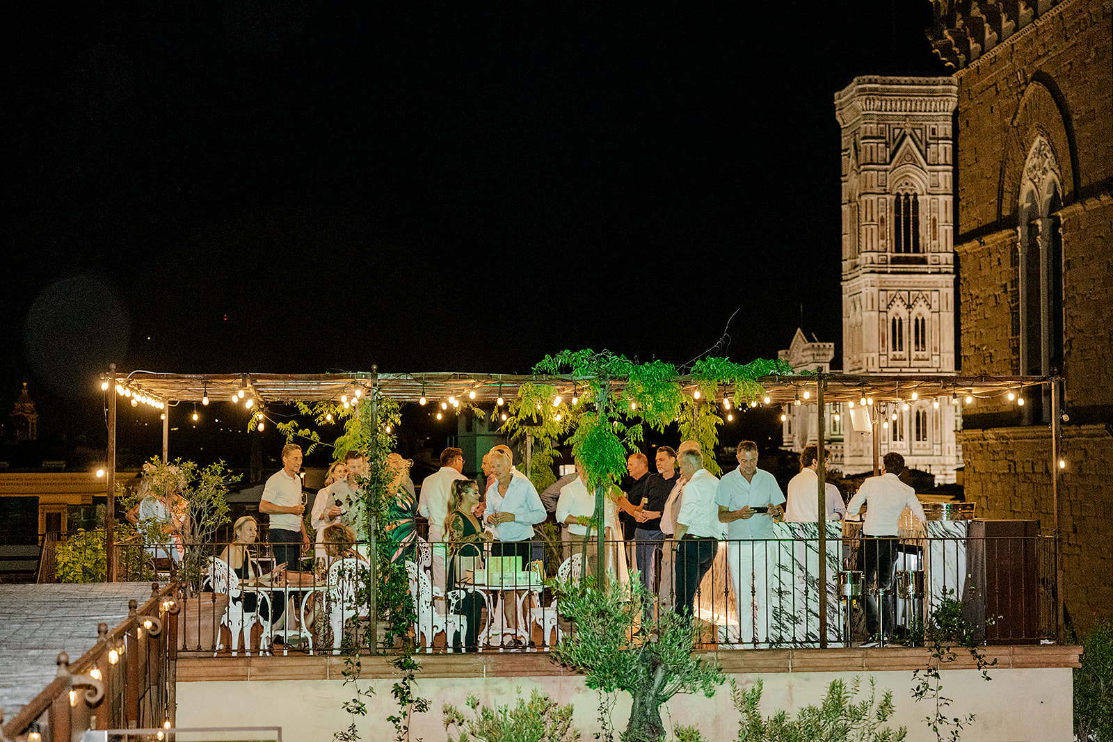 Guests celebrating on the Angel Roofbar terrace at night with the illuminated Duomo